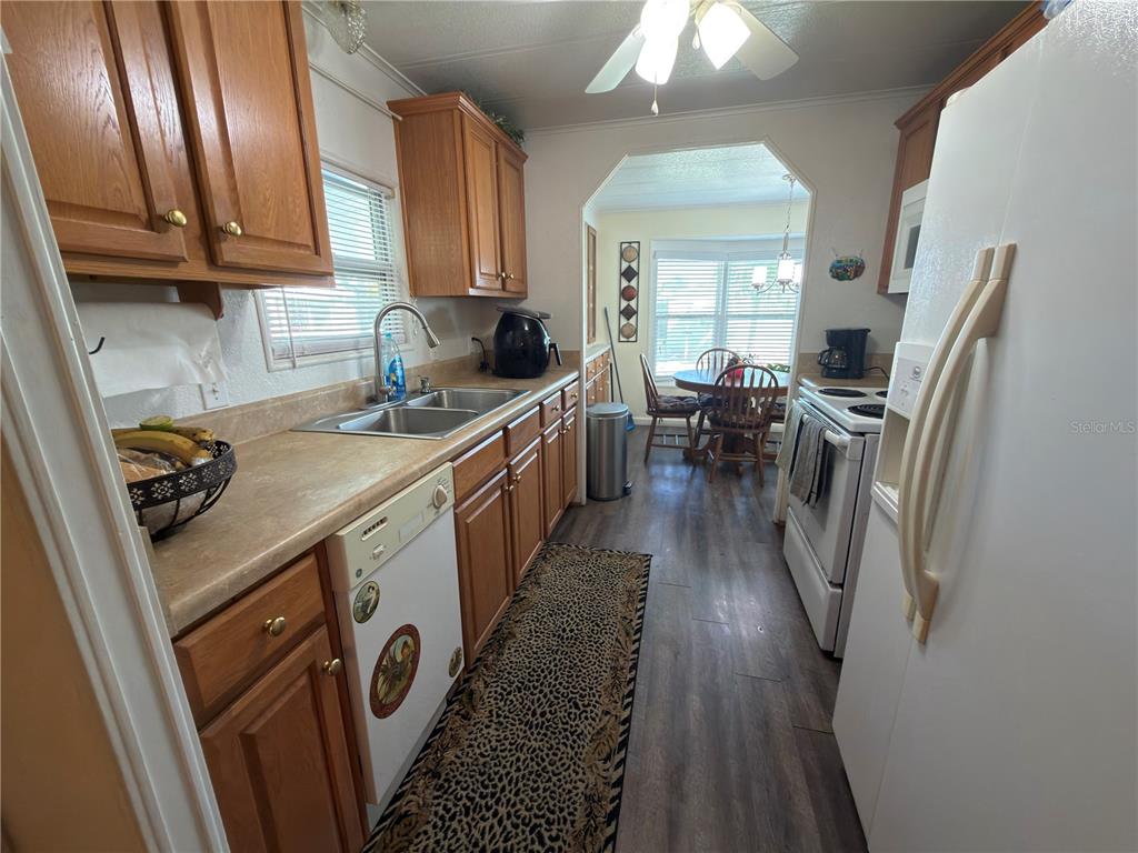 A kitchen with wood cabinets, laminate countertops, white appliances, and a dining area beyond — 2055 S FLORAL AVENUE UNIT 42, BARTOW, FL