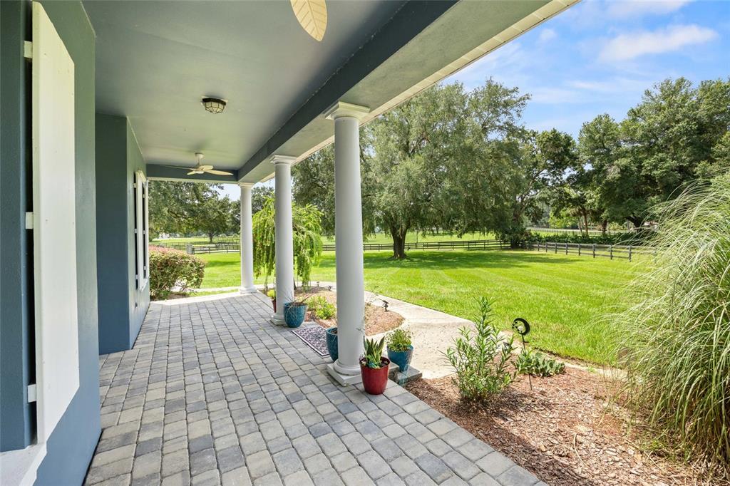A covered porch with stone pavers and white columns overlooks a grassy backyard with trees — 25 SE 69TH PLACE, OCALA, FL