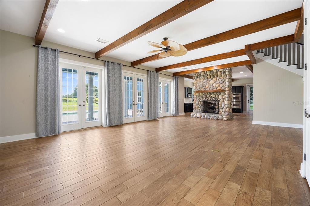 A spacious living room features wood-look flooring, exposed ceiling beams, and a stone fireplace — 25 SE 69TH PLACE, OCALA, FL