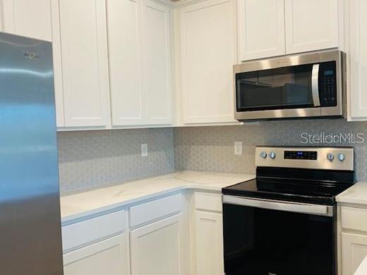 A kitchen features white cabinets, stainless steel appliances, and a light-colored countertop with backsplash — 4916 GULF WATERS DRIVE, NEW PORT RICHEY, FL