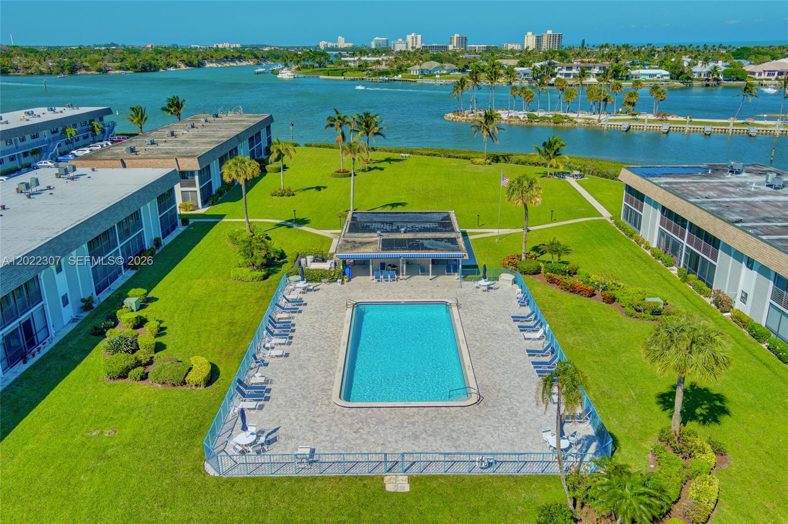 An aerial view shows a swimming pool and clubhouse surrounded by lawns and apartment buildings — 755 Saturn St # G202, Jupiter FL 33477, JUPITER, FL