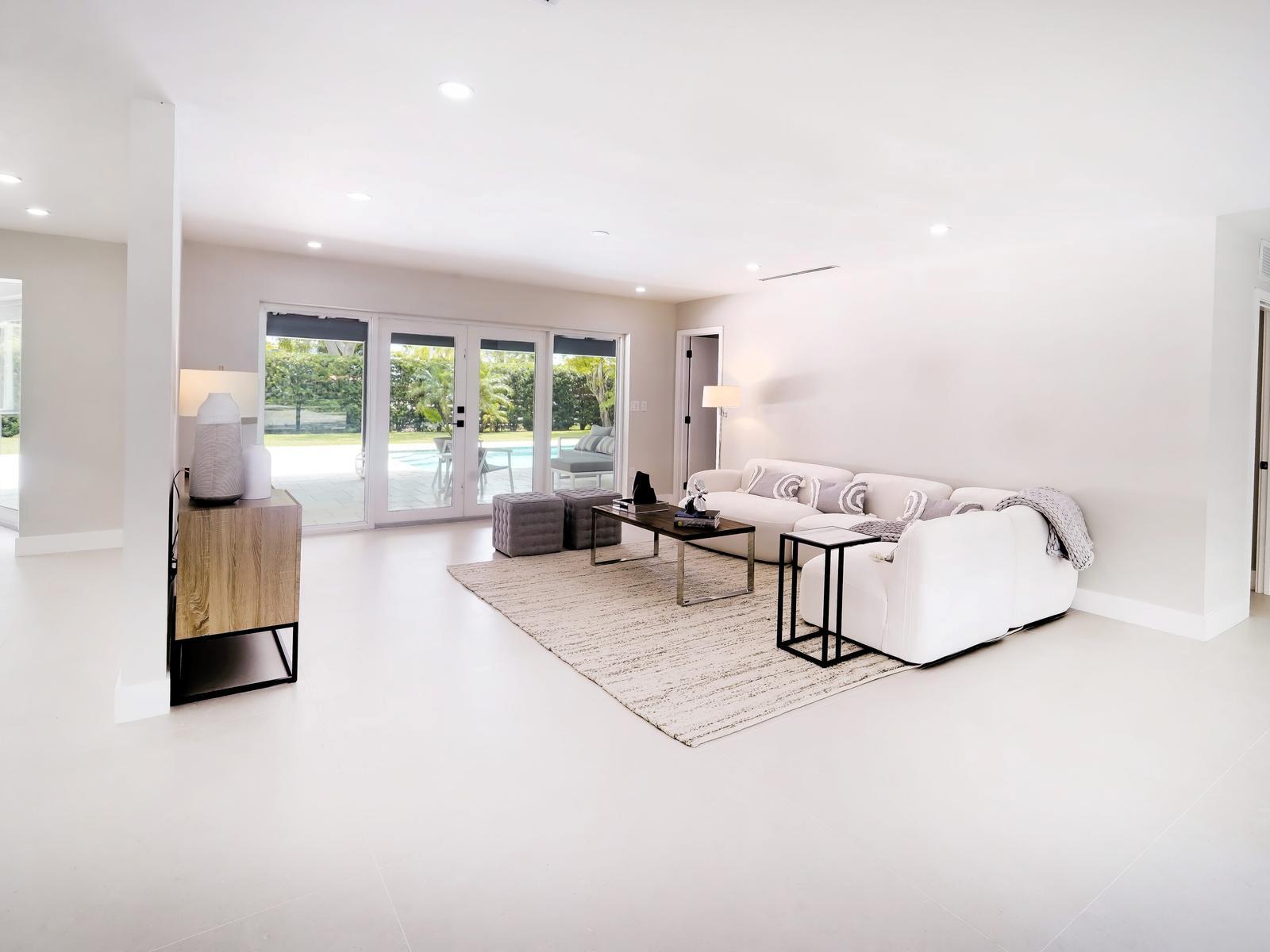 A bright living room features a white sectional sofa, a coffee table, and sliding glass doors — 12305 SW 73rd Avenue, Pinecrest FL 33156, PINECREST, FL