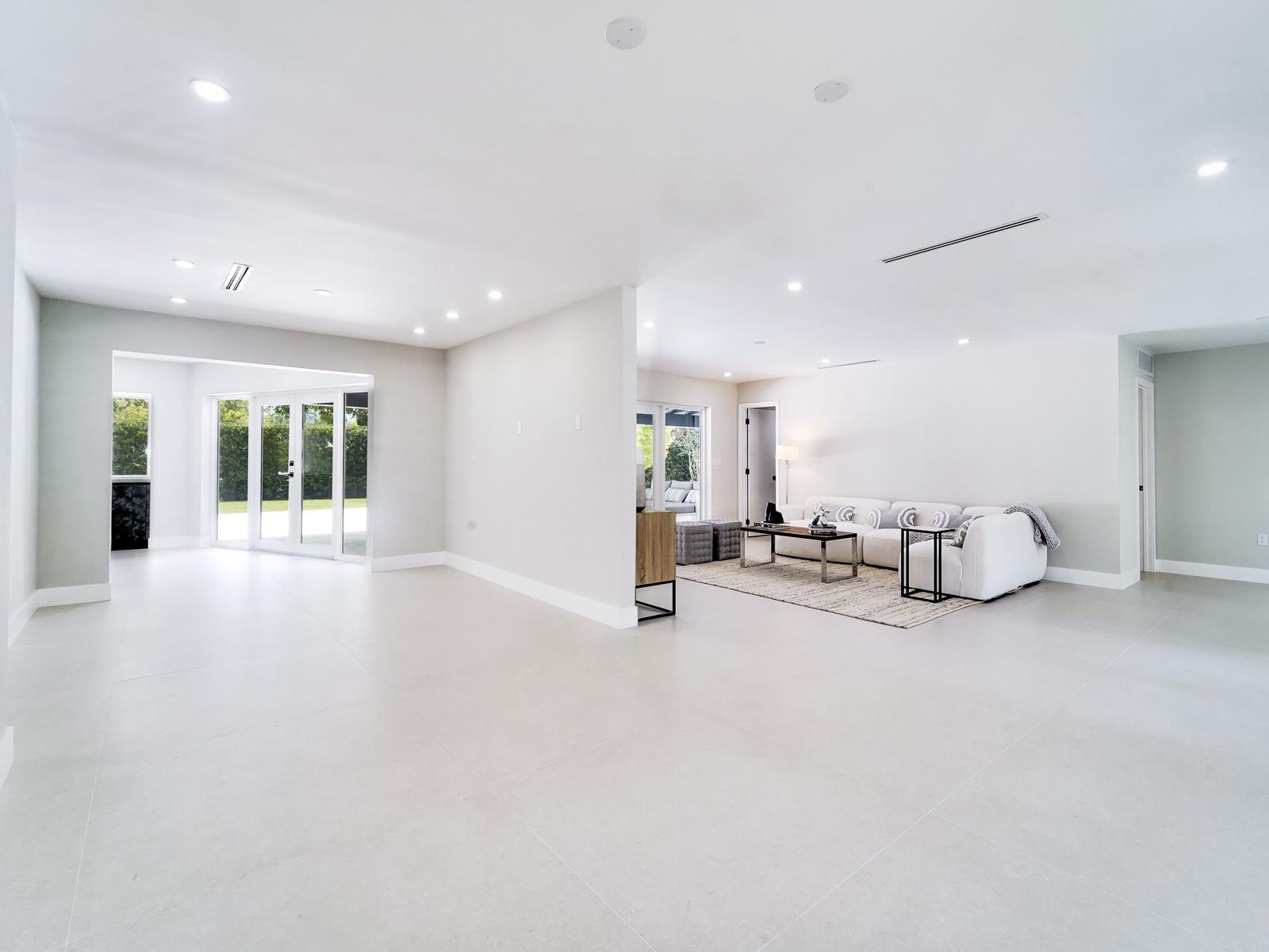 A spacious, minimalist living area features white tile floors, recessed lighting, and a neutral sofa — 12305 SW 73rd Avenue, Pinecrest FL 33156, PINECREST, FL