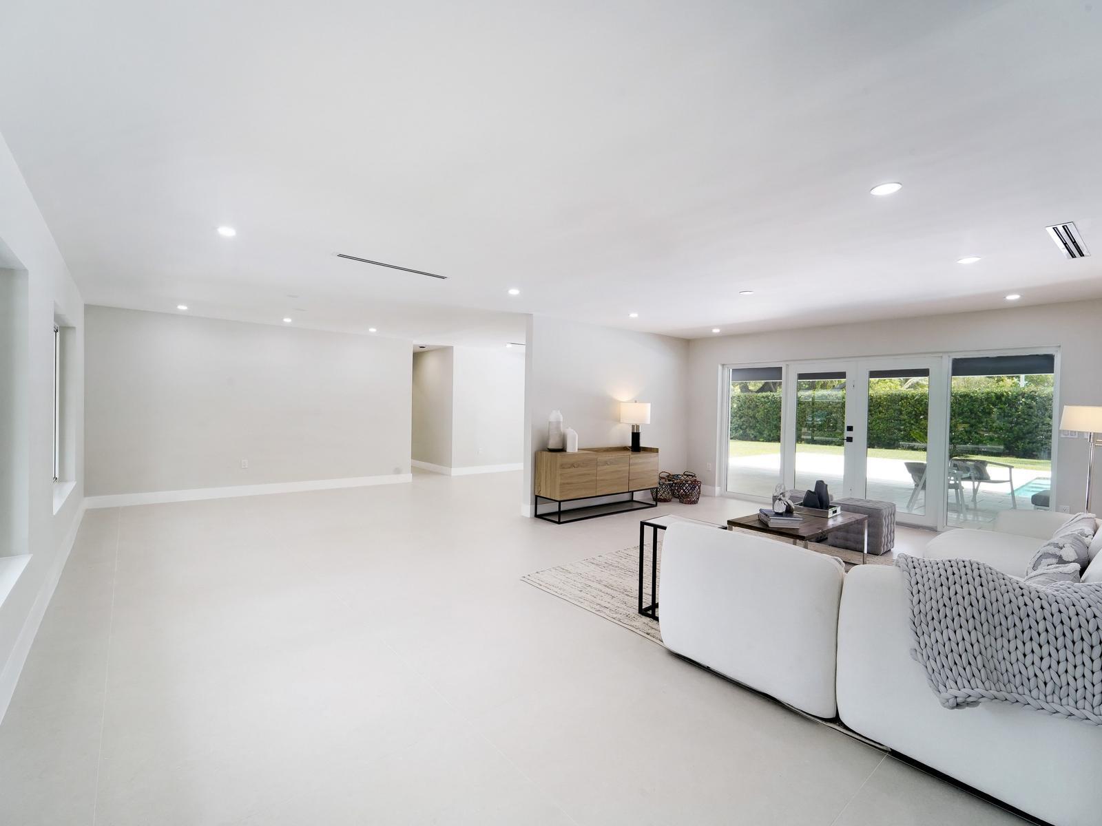 A bright, open-concept living room features white tile floors, a white sectional, and glass doors — 12305 SW 73rd Avenue, Pinecrest FL 33156, PINECREST, FL