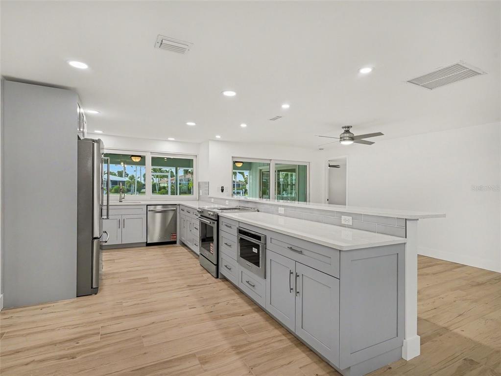 A modern kitchen features gray cabinets, white countertops, stainless steel appliances, and light wood flooring — 548 BELVEDERE COURT, PUNTA GORDA, FL