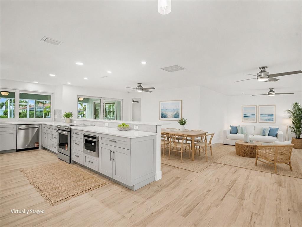 This virtually staged open-concept kitchen and living area features light wood floors and white cabinetry — 548 BELVEDERE COURT, PUNTA GORDA, FL