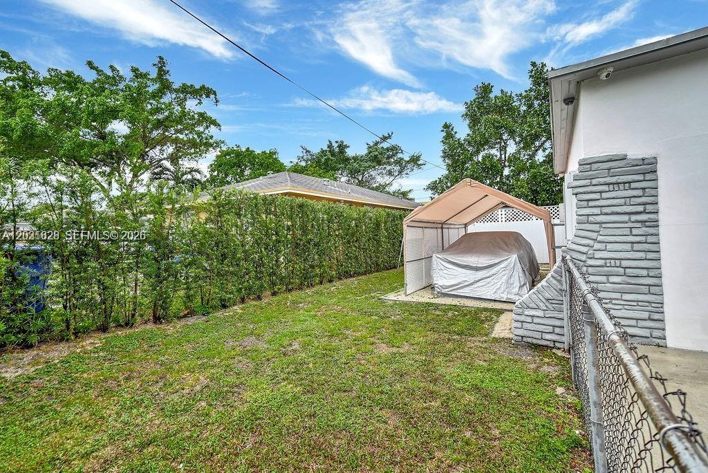 A backyard features a grass lawn, a hedge, and a covered car shelter — 600 NW 34th Ave, Miami FL 33125, MIAMI, FL