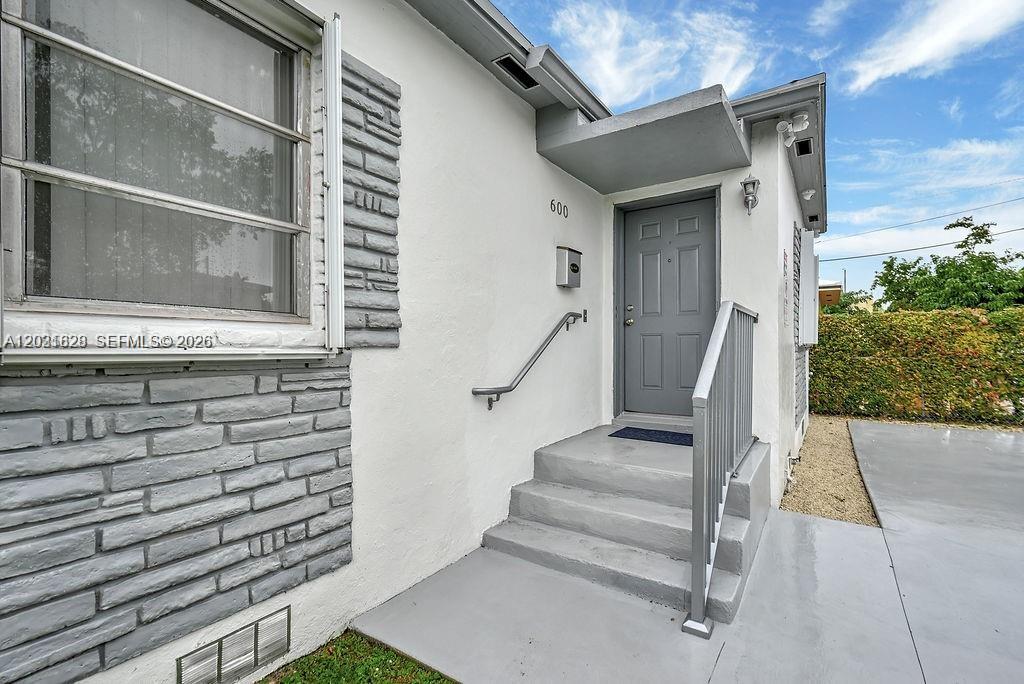 A gray front door with a metal railing and steps leads into a white house — 600 NW 34th Ave, Miami FL 33125, MIAMI, FL