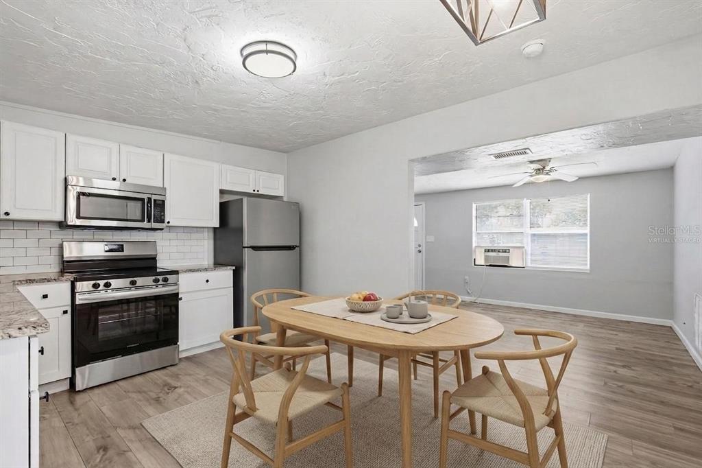 A kitchen and dining area with white cabinets, stainless steel appliances, and light wood flooring — 6727 SANDRA DRIVE, PORT RICHEY, FL