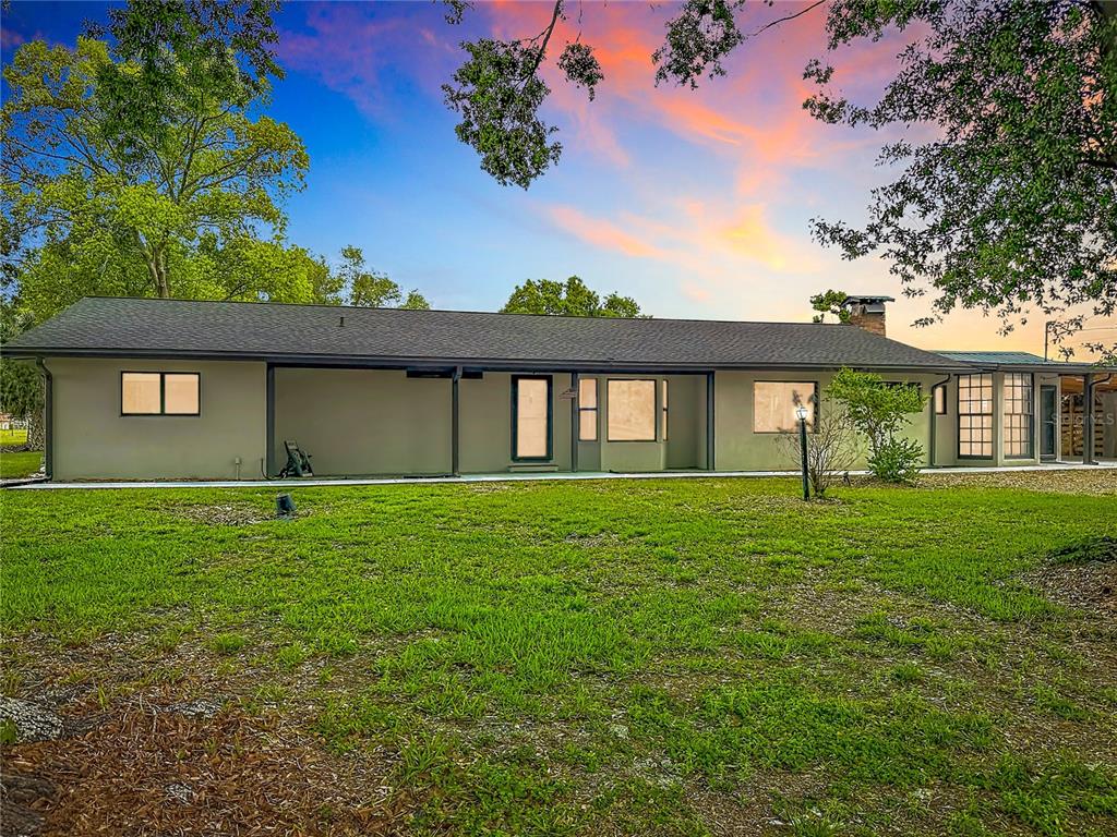 The rear exterior of a single-story house with a lawn and a sunset sky — 216 CORBETT ROAD, LITHIA, FL