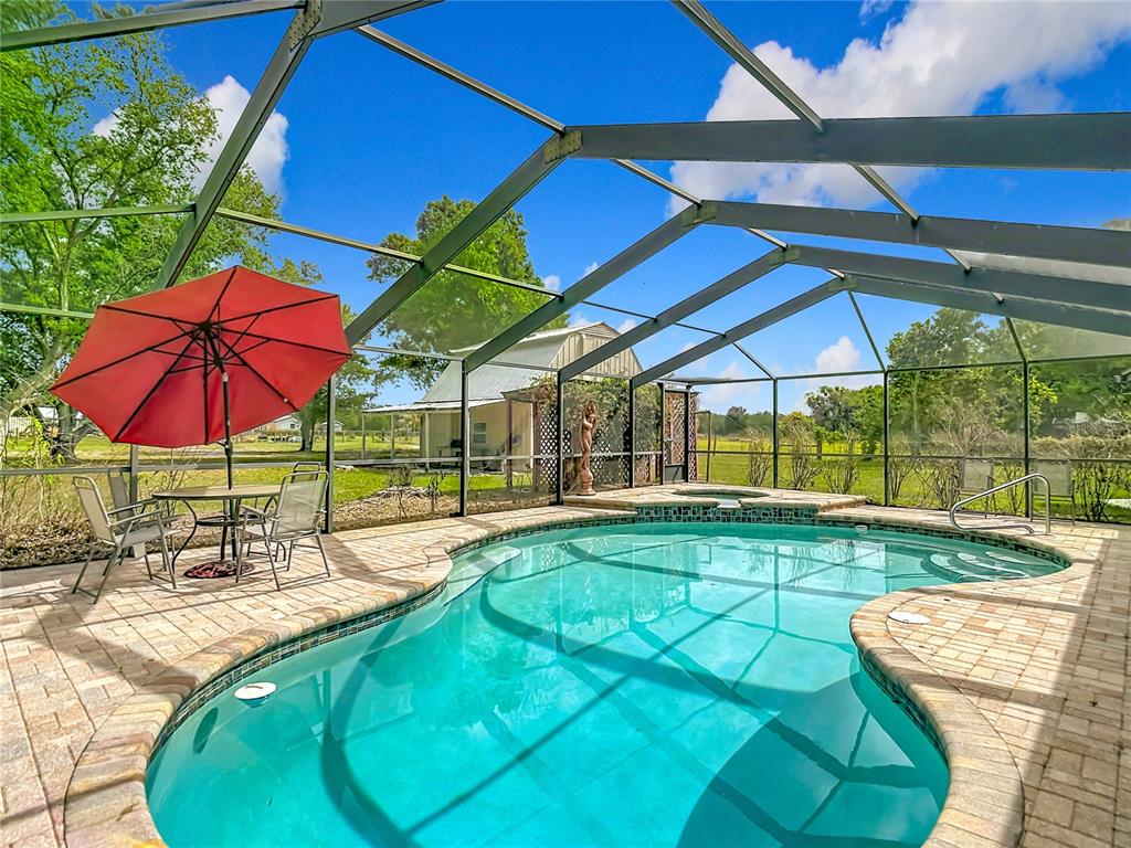A screened-in swimming pool with a patio, red umbrella, and a detached building in back — 216 CORBETT ROAD, LITHIA, FL