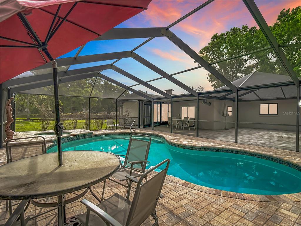 A screened-in patio features a swimming pool, brick pavers, and outdoor furniture at sunset — 216 CORBETT ROAD, LITHIA, FL