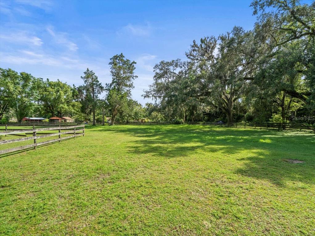 A grassy field is enclosed by a wooden fence with large trees in the background — 18750 KUKA LANE, SPRING HILL, FL