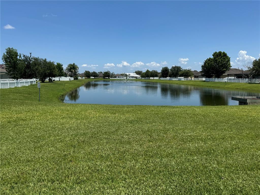 A grassy lawn leads to a pond with a fountain, surrounded by houses and fences — 3711 BRIARWOOD ESTATES CIRCLE, ST CLOUD, FL