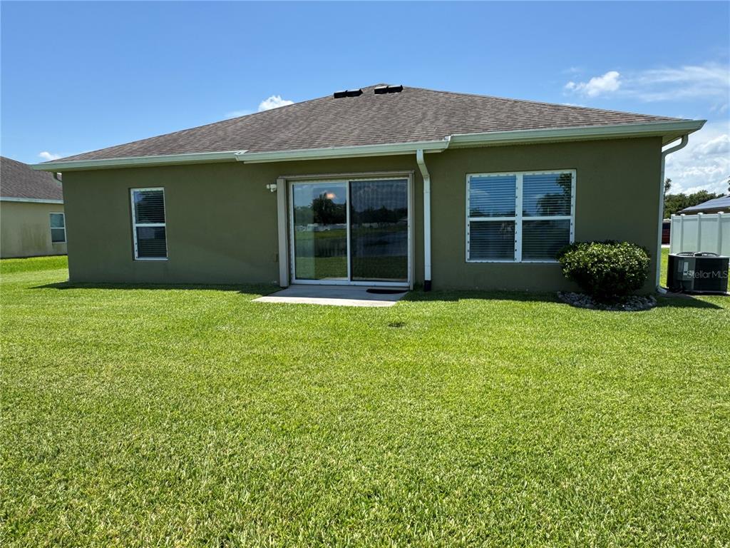 The rear exterior of a single-story house features a sliding glass door and lawn — 3711 BRIARWOOD ESTATES CIRCLE, ST CLOUD, FL