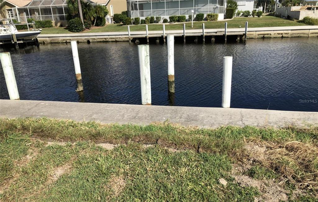 A concrete seawall borders a canal with several white mooring pilings in the water — 3754 SPOONBILL COURT, PUNTA GORDA, FL