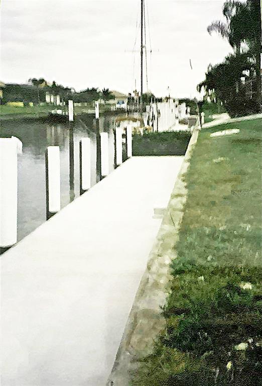 A concrete dock runs alongside a grassy lawn next to a canal with boat slips — 3754 SPOONBILL COURT, PUNTA GORDA, FL
