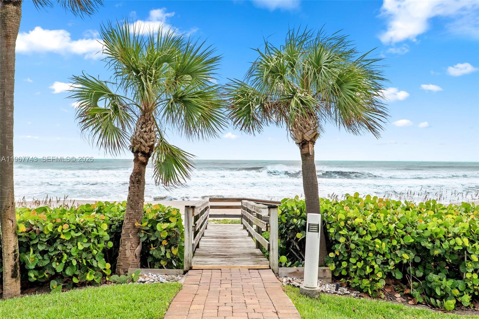 A brick walkway leads to a wooden boardwalk between two palm trees facing the ocean — 601 N Miramar # 107, Indialantic FL 32903, INDIALANTIC, FL