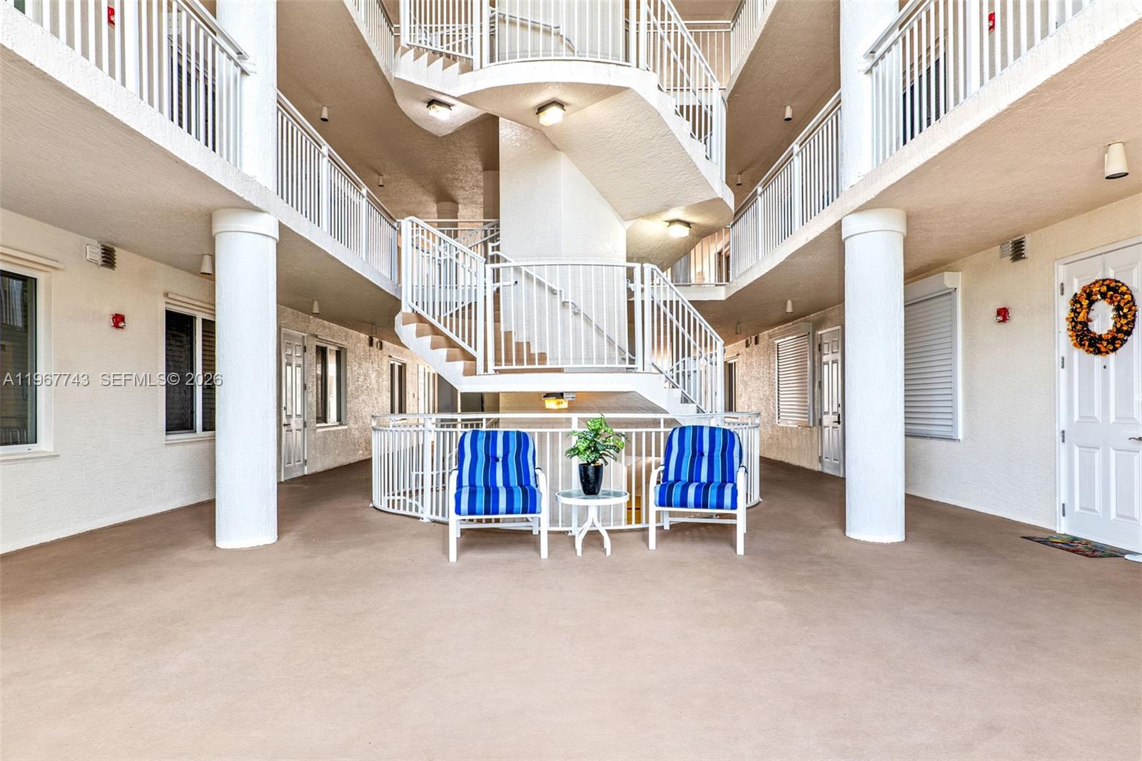An open-air apartment building corridor features a central spiral staircase and two blue-striped chairs — 601 N Miramar # 107, Indialantic FL 32903, INDIALANTIC, FL