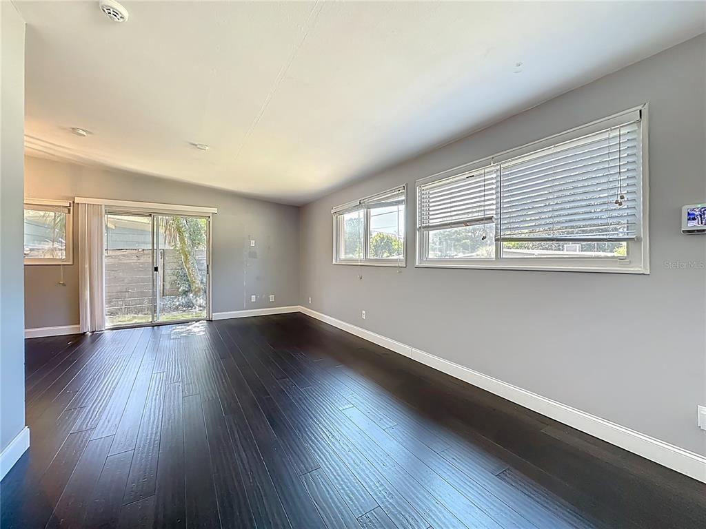 An empty room features dark wood flooring, light gray walls, and several windows — 7615 MAYAPPLE ROAD, JACKSONVILLE, FL