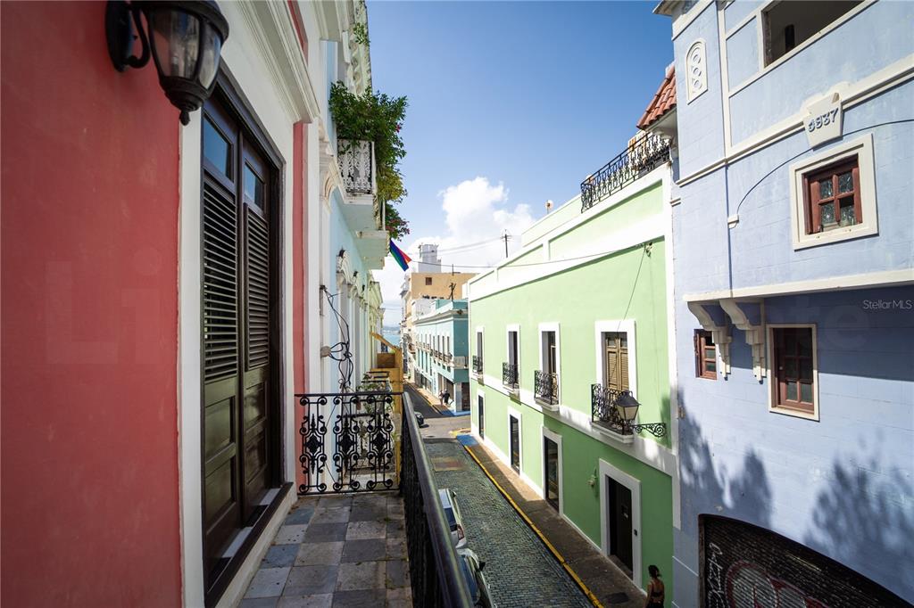 A view from a balcony overlooking a narrow cobblestone street lined with colorful historic buildings — 153 SAN JUSTO, SAN JUAN, PR
