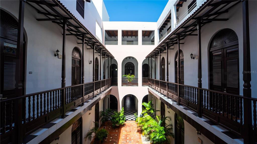 An open-air courtyard features multi-level balconies with dark wooden railings and arched doorways — 153 SAN JUSTO, SAN JUAN, PR