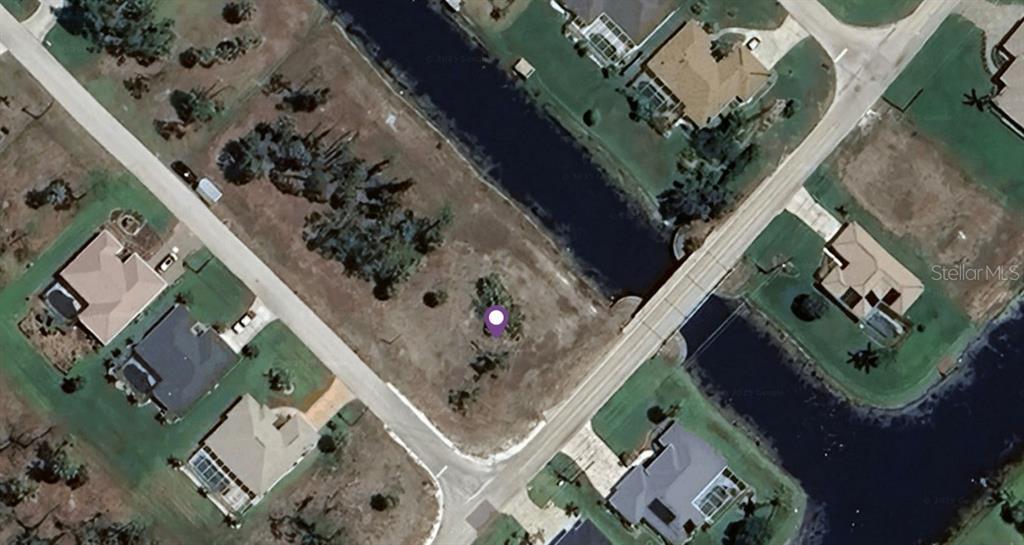 This aerial view shows a vacant, tree-dotted residential lot situated between two roads and a canal — 1026 ROTONDA CIRCLE, ROTONDA WEST, FL