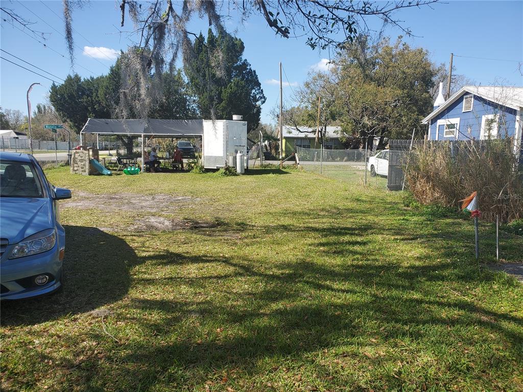A grassy yard features a covered patio area with a trailer and a blue house — 2213 W PARKER STREET, LAKELAND, FL