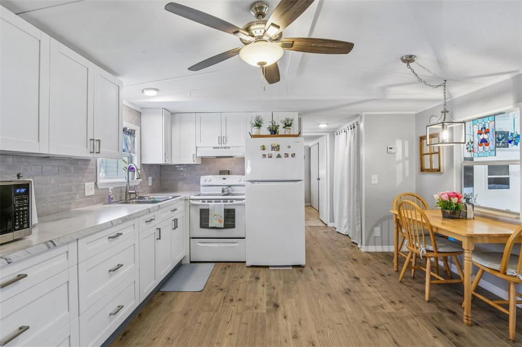 A kitchen with white cabinets, stainless steel appliances, and a dining table on wood flooring — 3204 POND HOLLOW STREET, WESLEY CHAPEL, FL