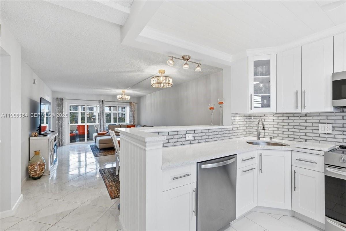 A white kitchen with a breakfast bar overlooks a living area with tile floors — 3201 NE 8th St # 405, Pompano Beach FL 33062, POMPANO BEACH, FL