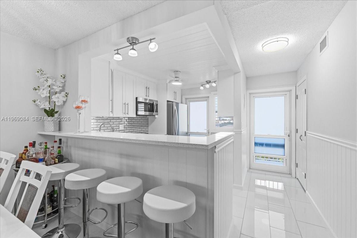 A white kitchen features a breakfast bar with stools, tile flooring, and stainless steel appliances — 3201 NE 8th St # 405, Pompano Beach FL 33062, POMPANO BEACH, FL