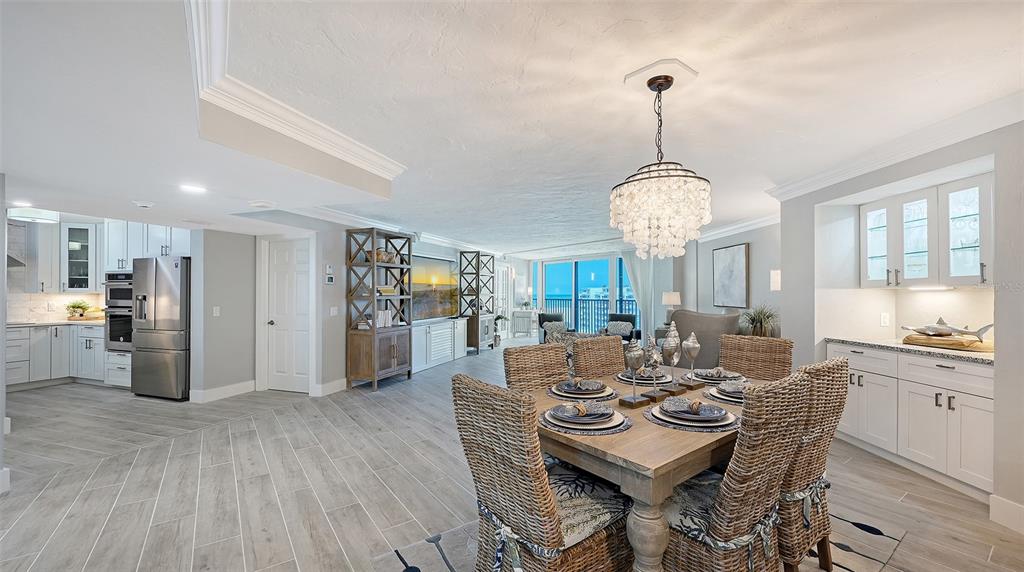 A dining area with wicker chairs sits adjacent to a modern kitchen and living space — 5880 MIDNIGHT PASS ROAD UNIT 907, SARASOTA, FL