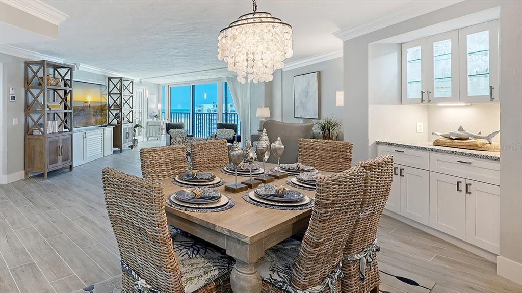 A dining room features a wooden table with wicker chairs beneath a large shell chandelier — 5880 MIDNIGHT PASS ROAD UNIT 907, SARASOTA, FL