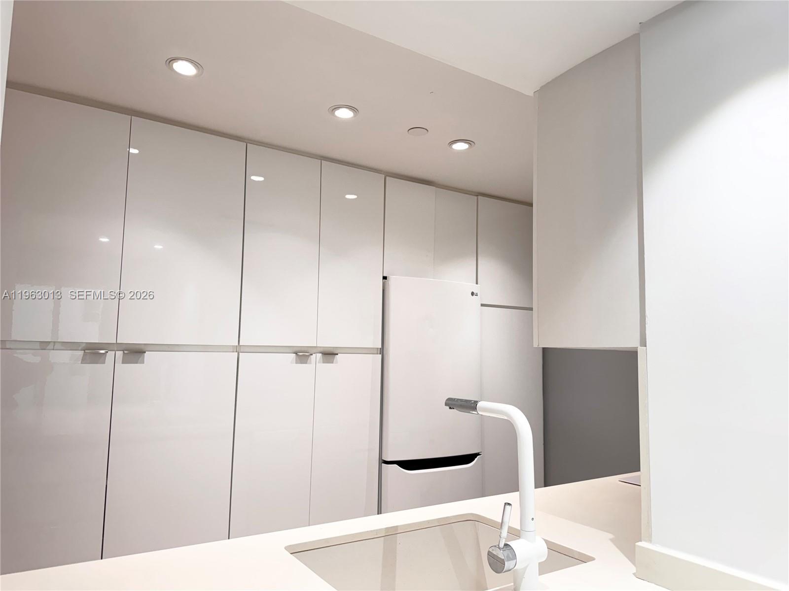 A modern kitchen features white glossy cabinetry, a white faucet, and a built-in refrigerator — 1200 West Ave # 1418, Miami Beach FL 33139, MIAMI BEACH, FL