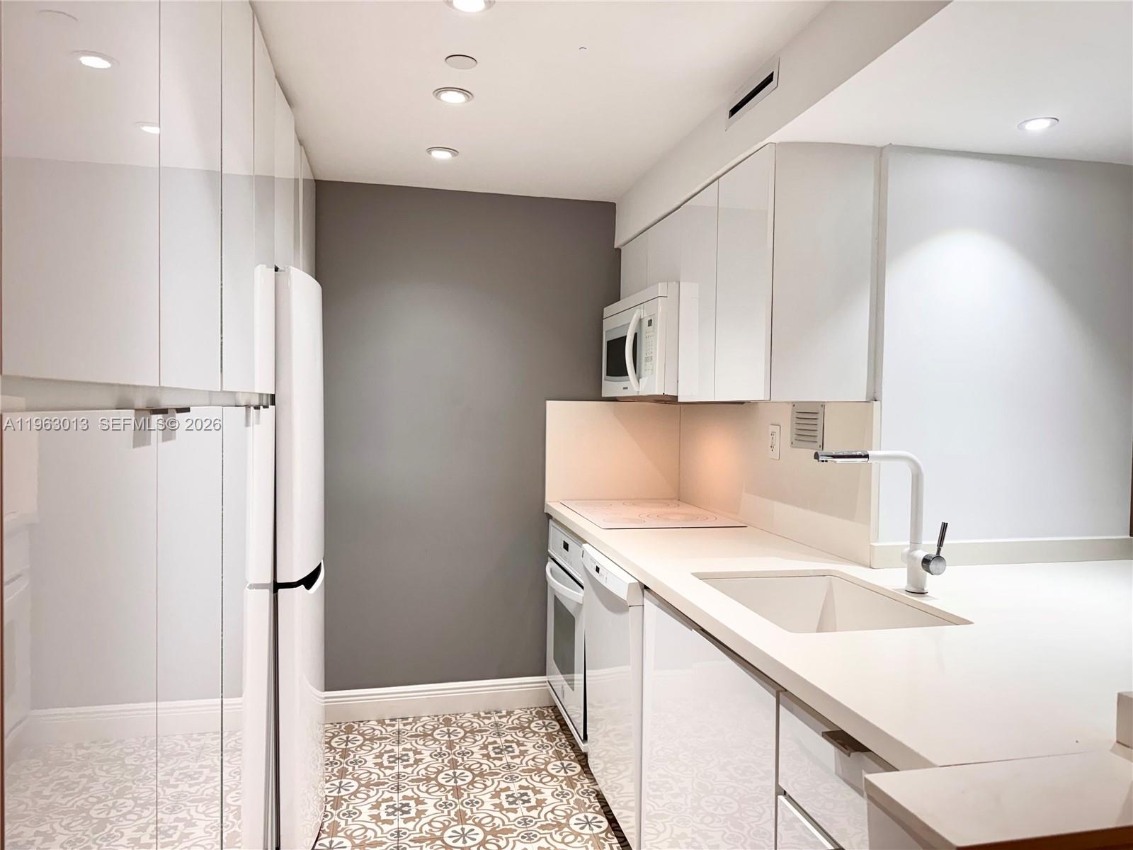 A galley kitchen features white cabinetry, a white refrigerator, and patterned tile flooring — 1200 West Ave # 1418, Miami Beach FL 33139, MIAMI BEACH, FL