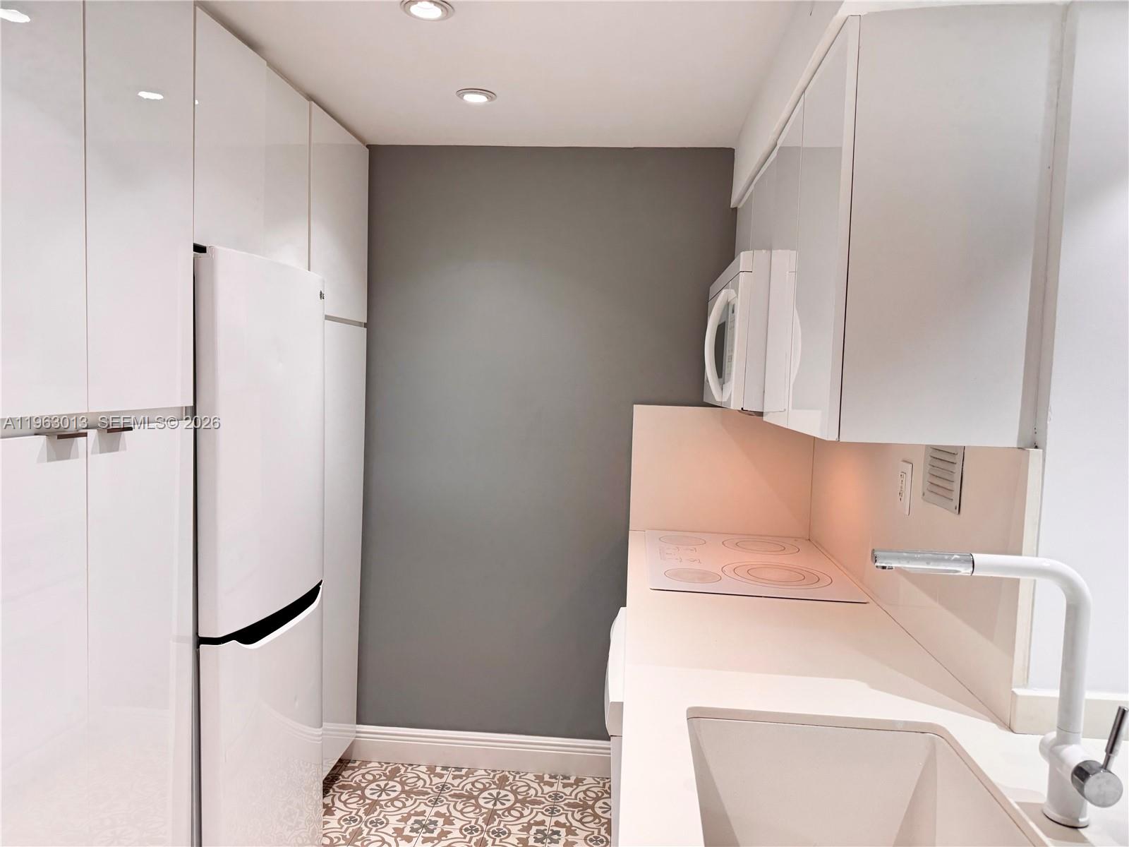 A compact kitchen features white cabinetry, a white refrigerator, a cooktop, and patterned floor tiles — 1200 West Ave # 1418, Miami Beach FL 33139, MIAMI BEACH, FL