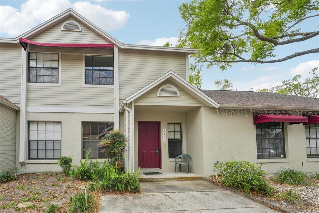 A two-story house with beige siding, a red front door, and red window awnings — 8419 LAURELON PLACE, TEMPLE TERRACE, FL