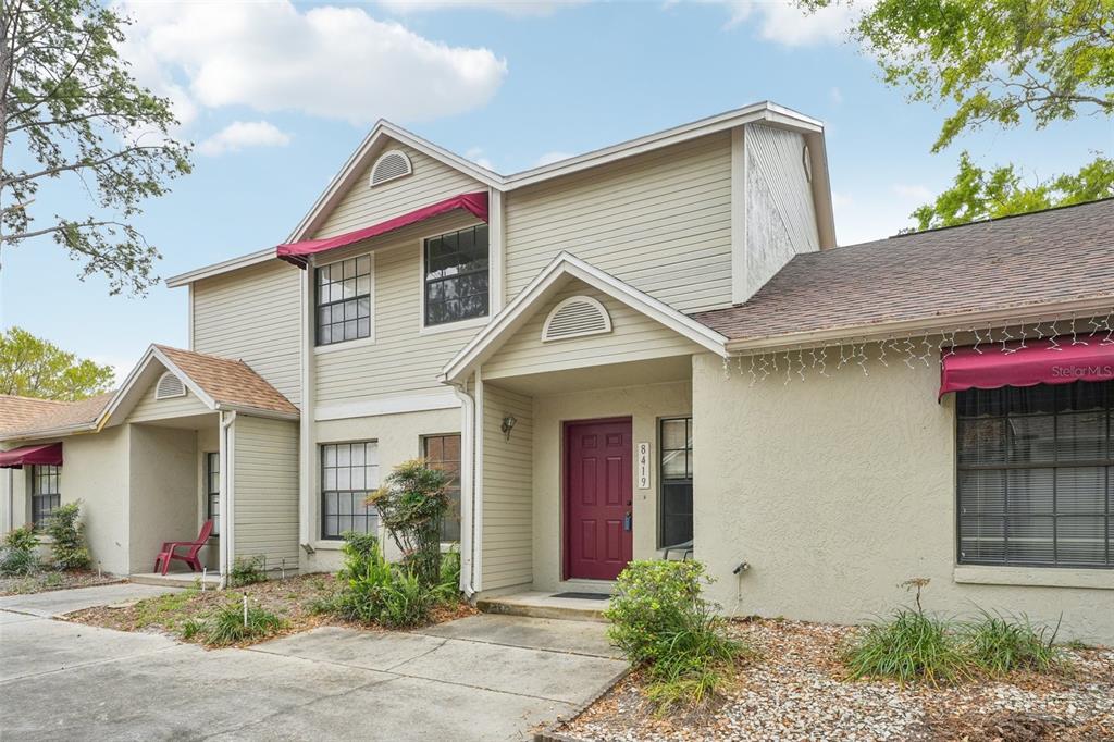 A two-story townhouse exterior features beige siding, a red front door, and red window awnings — 8419 LAURELON PLACE, TEMPLE TERRACE, FL