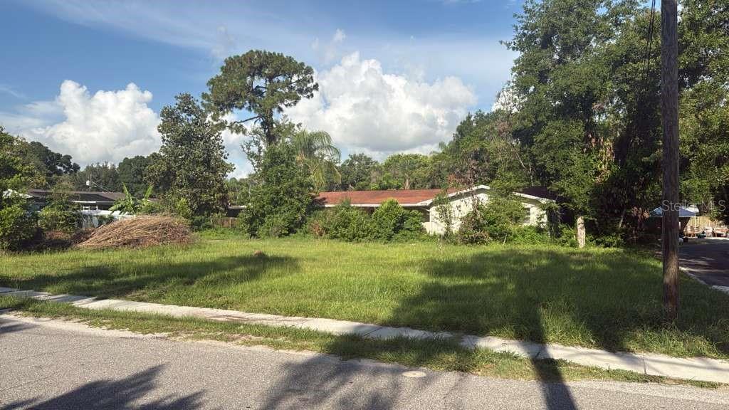 A vacant, grassy lot sits in front of a single-story house with a red roof — 12706 N 53RD STREET, TAMPA, FL