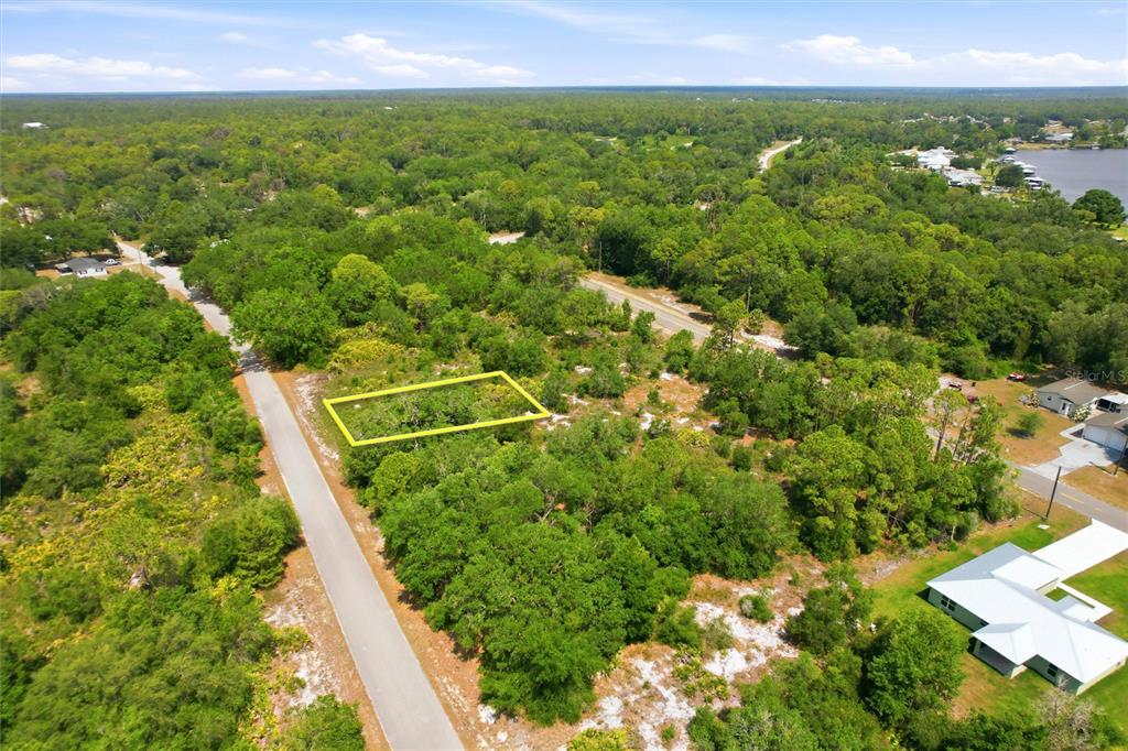 An aerial view shows a vacant, wooded lot outlined in yellow next to a paved road — 3392 GOSSAMER AVENUE, LAKE PLACID, FL