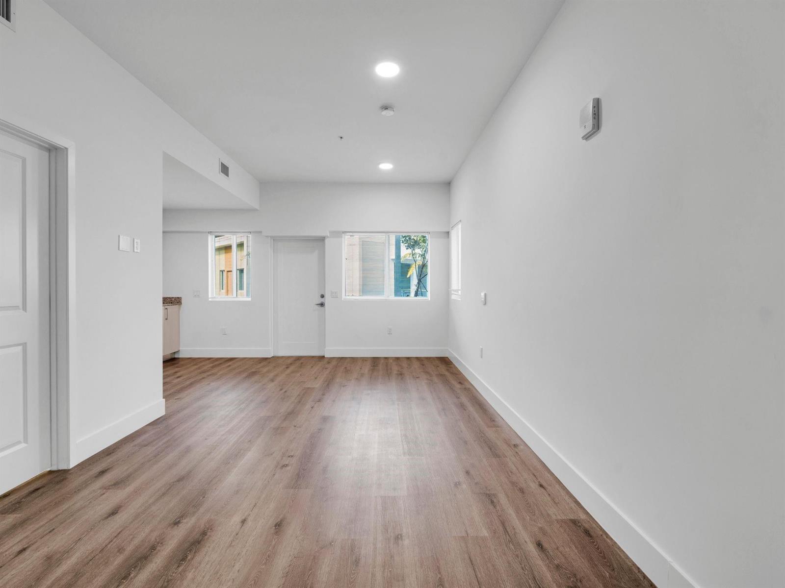An empty room with white walls, wood-look flooring, two windows, and a white door — 2130 NW 37th Street, Miami FL 33142, MIAMI, FL