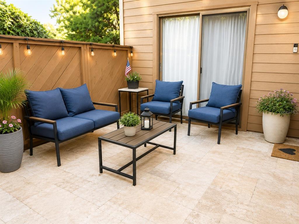 A patio features a sofa, two chairs, a coffee table, and string lights against a fence — 1503 LENNOX ROAD E UNIT 1503, PALM HARBOR, FL