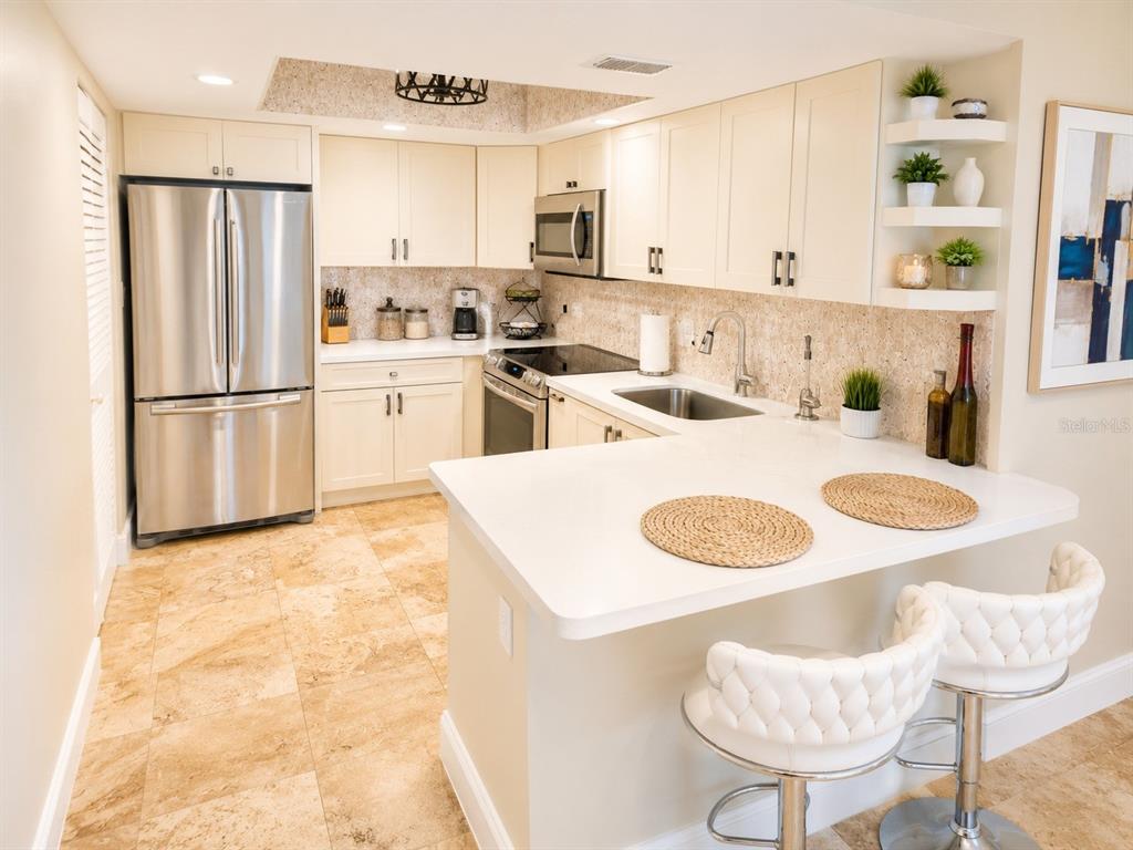 A kitchen features light-colored cabinets, stainless steel appliances, a breakfast bar, and tiled flooring — 1503 LENNOX ROAD E UNIT 1503, PALM HARBOR, FL
