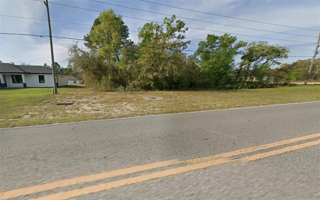 A vacant, grassy residential lot sits beside a paved road with trees in the background — 2470 W CITRUS SPRINGS BOULEVARD, CITRUS SPRINGS, FL