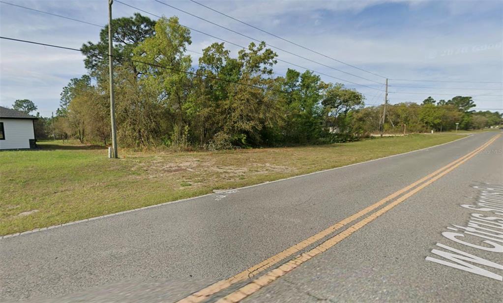 A vacant, grassy lot with trees sits beside a paved road under a blue sky — 2470 W CITRUS SPRINGS BOULEVARD, CITRUS SPRINGS, FL