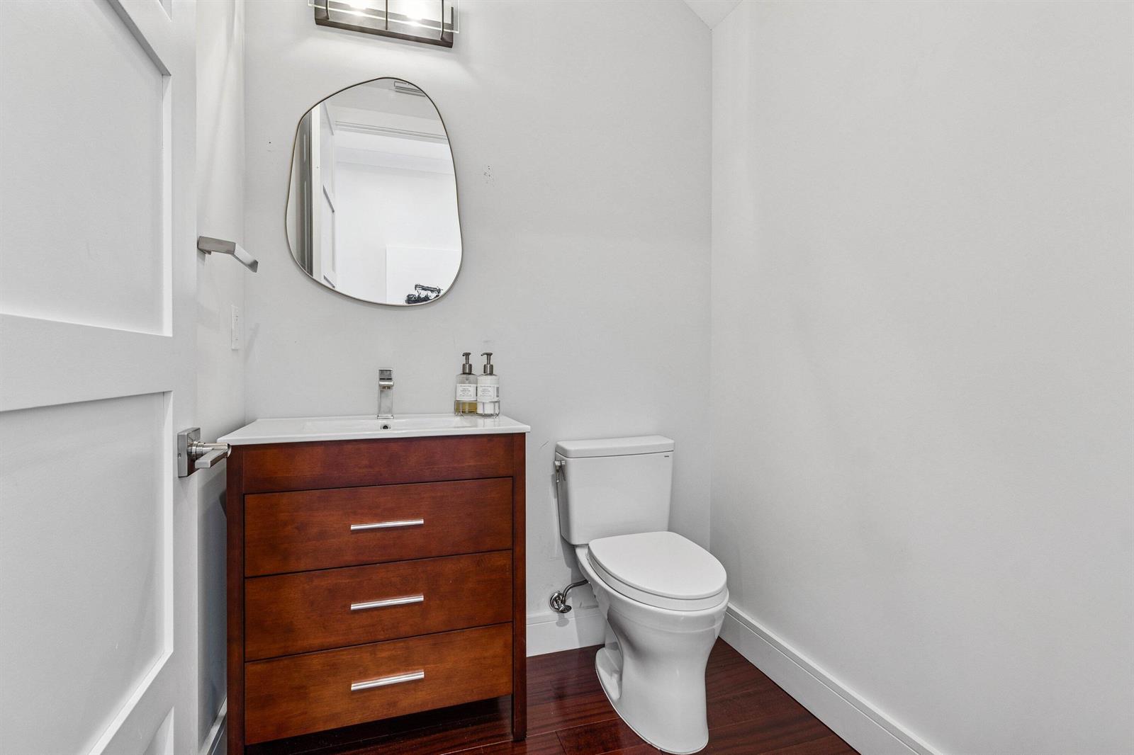 A small bathroom features a wooden vanity, an organic-shaped mirror, and a white toilet — 412 SE 4th Avenue, Delray Beach FL 33483, DELRAY BEACH, FL
