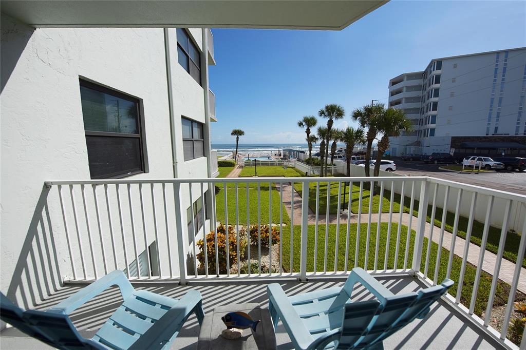 A balcony with two blue chairs overlooks a grassy courtyard, palm trees, and the ocean — 1571 S ATLANTIC AVENUE UNIT 202, NEW SMYRNA BEACH, FL