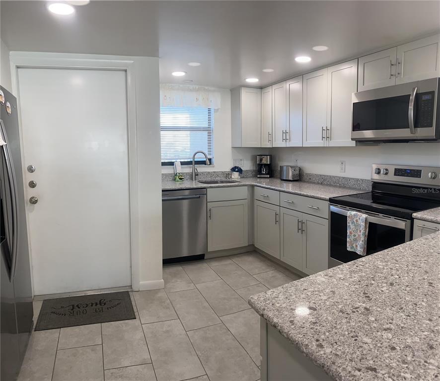 A kitchen features light gray cabinets, granite countertops, stainless steel appliances, and tile flooring — 1571 S ATLANTIC AVENUE UNIT 202, NEW SMYRNA BEACH, FL