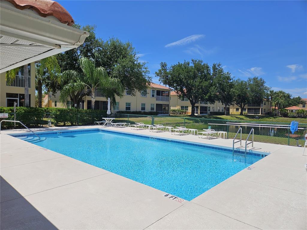 A rectangular swimming pool sits on a concrete deck in front of apartment buildings — 904 CASA DEL LAGO WAY UNIT 904, VENICE, FL