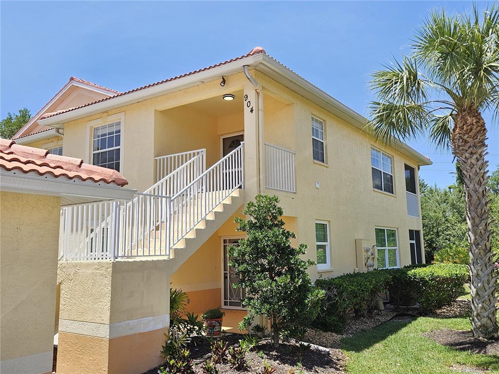 A two-story yellow stucco building features an exterior staircase leading to an upper-level entrance — 904 CASA DEL LAGO WAY UNIT 904, VENICE, FL